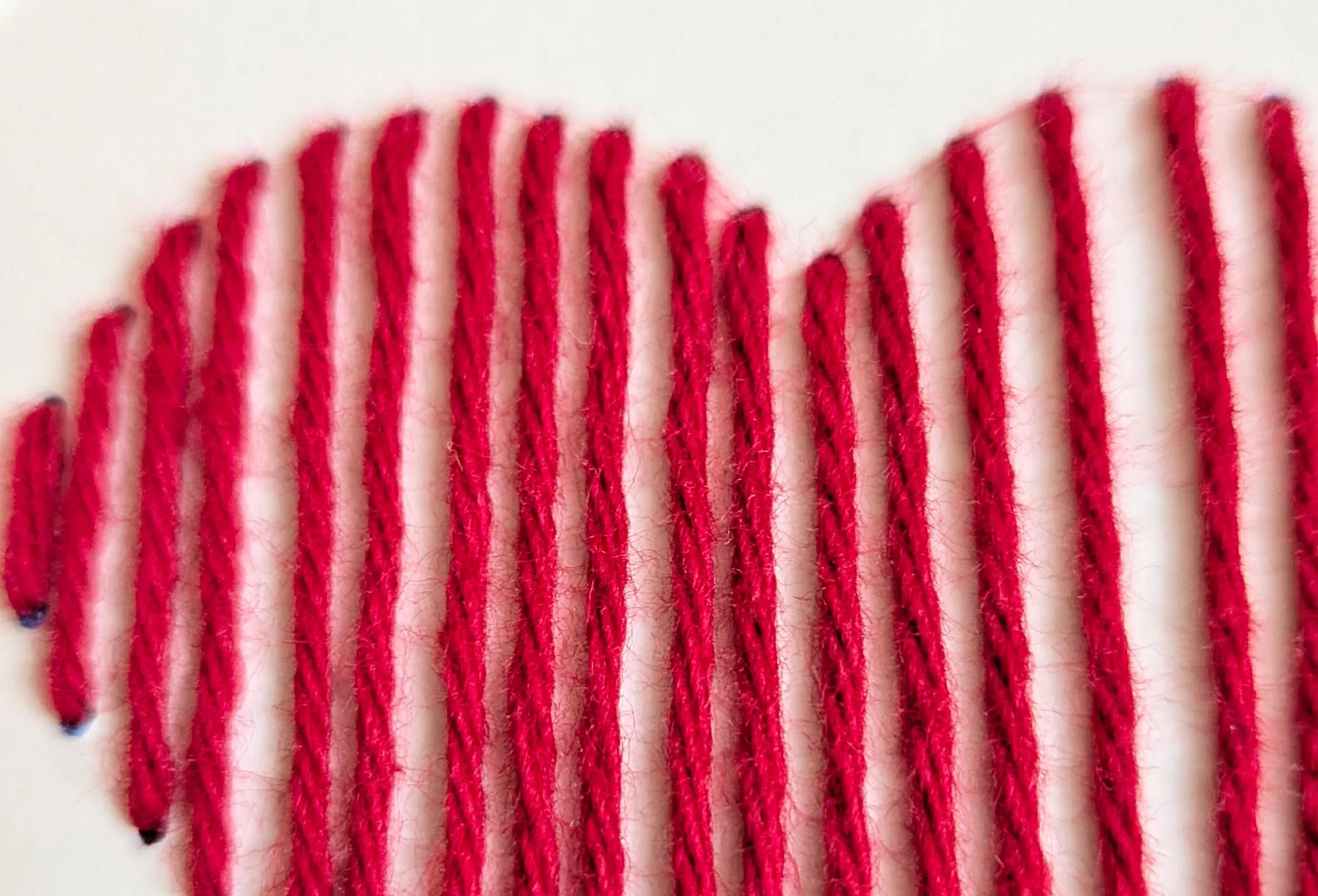 Nahaufnahme: rotes Garn, von Hand zu einem Herz gestickt